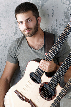 Mann mit kurzem braunen Haar und braunem Vollbart hat Gitarre mit zwei Hälsen um den Körper geschnallt.