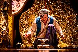 Zu sehen ist eine Bühnenszene aus Aladin und die Wunderlampe. Aladin kniet vor der goldenen Öllampe. Der Hintergrund ist gold.