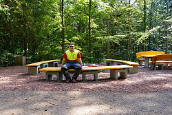 Der Auszubildende Björn Schaub sitzt auf der Bank, die er selbst hergestellt hat. Sie besteht aus einer langen Holzplatte, die Füße sind aus Stein.