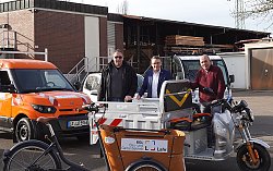 Auf dem Bild sind zu sehen von links nach rechts: BGL Fuhrparkleiter Patrick Obergföll, Oberbürgermeister Markus Ibert und BGL-Leiter Herbert Schneider mit der E-Mobil Flotte des BGL. Sie stehen mit den Fahrzeugen im Hof des Bau- und Gartenbetriebs. Die Sonne scheint.