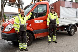 Thomas Wieseke und Harald Mark mit der neuen BGL-Dienstkleidung. Jacken und Hosen sind schwarz und signalgelb mit Reflektoren. Hinter ihnen steht ein Transporterfahrzeug des BGL.