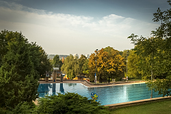 Das Foto zeigt das Schwimmerbecken mit den Sprungtürmen des Lahrer Terrassenbads mit den grünen Bäumen und den liegen Wiesen.