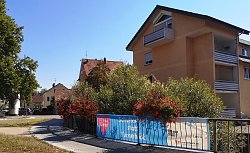 Ein Banner mit der Aufschrift &#34;Schulterblick statt Tunnelblick&#34; hängt an einem Brückengeländer. Im Hintergrund Wohnhäuser, ein Gehweg und grüne Sträucher.