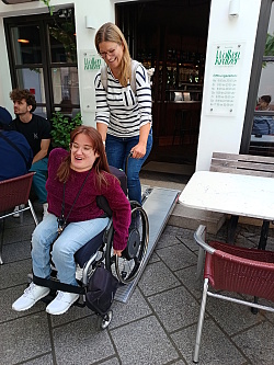 Frau schiebt Rollstuhlfahrerin über eine mobile Rampe aus einem Café
