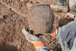 Ein Archäologe hält bei einer Ausgrabung eine Urne aus der Römerzeit in behandschuhten Händen.