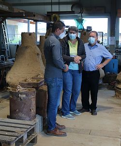 Ein Glockengießer im Gespräch mit zwei Besuchern, links eine Glockenform