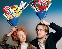 Eine rothaarige Frau und ein dunkelblonder Mann halten sich blaue Trichter über den Kopf. In diesn Trichtern sieht man Ausschnitte aus bekannten Zeitungen und Magazinen.