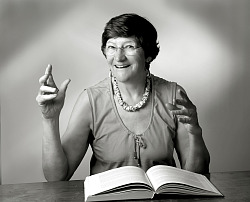 Die Autorin sitzt an einem Tisch, vor sich ein Buch und sie gestikuliert mit beiden Armen. 