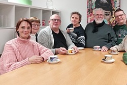 Eine Gruppe von Menschen sitzt mit Kaffeetassen gemeinsam am Tisch