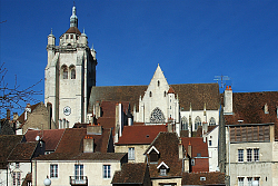 Das Bild zeigt die Stiftskirche Notre-Dame in Dole von der Seite. Das imposante Gebäude im gotischen Stil liegt auf einem Hügel und ragt daher weiter über die umliegenden Häuser hinaus. Links ist der Turm zu erkennen, rechts das Kirchenschiff.