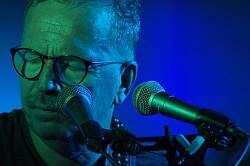 Musiker mit geschlossenen Augen am Mikrofon, blauer Hintergrund