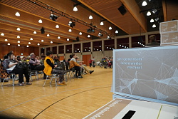 Gestapelte Abstimmungsurnen, im Hintergrund sitzende Zuhörer während der Live-Auszählung im Oktober 2023