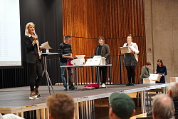 Frau Dewes moderiert die Live-Auszählung am Tag der Entscheidung 2023 während städtische Mitarbeitende die Auszählung pro Abstimmungsurne vornehmen