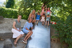 Das Foto zeigt drei Frauen und sechs Kinder, die an und auf einer Rutschbahn stehen. Alle freuen sich und haben teilweise die Hände nach oben gestreckt.