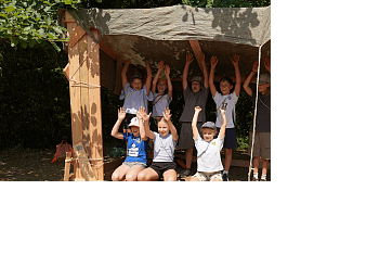 Gruppe von Kindern sitzt und steht in einem selbstgebauten Holzrahmen mit Tuchdach und hebt die Arme
