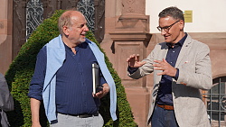 Auf dem Bild sind Markus Ibert und Dr. Haiko Holland  zu sehen. Herr Ibert trägt ein blaues Hemd und ein beiges Jackett. Herr Dr. Holland ein blaues Hemd und eine hellblaue Weste um die Schultern. Im Hintergrund ist die Dinglinger Kirche zu sehen. 