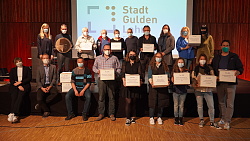 Gewinnerinnen und Gewinner mit ihren Abstimmungsboxen auf der Bühne, Oberbürgermeister Markus Ibert hält eine große goldene Münze