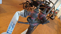 Eine alte Pumpe, die in der Ausstellung vor einem alten Pumpenwagen steht. 