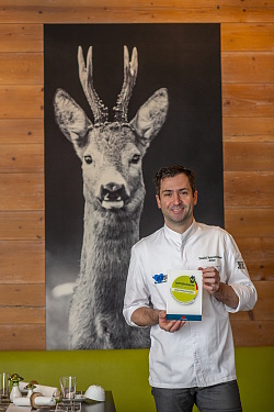 Daniel Fehrenbacher mit dem Zertifikat des deutschen Wanderverbandes vor dem Schwarz-Weiß-Bild eines Rehs