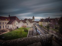 Blick auf die Stadt Dole in der Abenddämmerung, zu sehen sind historische Gebäude mit roten Ziegeldächern, ein Kirchturm und eine von Bäumen gesäumte Straße