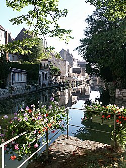 Blick auf eine idyllische Häuserfront mit vielen Blumenkästen am Geländer des Kanals in Dole