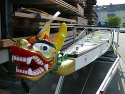 Das Bild zeigt das Lahrer Drachenboot mit einem großen Drachenkopf am Bug. Der Drache glänzt golden, hat gelbe Hörner und einen großen roten Mund mit weißen Zähnen