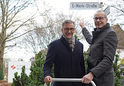 Lahrs Oberbürgermeister Markus Ibert und Bernhard Palm, Vorstand E-Werk Mittelbaden, präsentieren das neue Schild der E-Werk-Straße. Beide sind winterlich angezogen. Herr Palm deutet auf das neue Schild. 