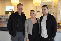 Zwei Männer und eine Frau vor der Theke im Innenraum eines Cafés.