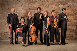 Ensemble Aventure: sieben Musikerinnen und Musiker in schwarzer Kleidung mit Instrumenten vor einer Steinmauer