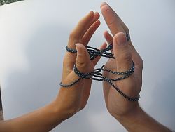 Das Foto zeigt die rechte und linke Hand einer Person. Die Handinnenflächen zeigen zueinander. Um die einzelnen Finger ist ein dickerer Faden gewunden.