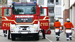 Ein Feuerwehrauto von vorne mit geöffneten Türen links und rechts, zwei Feuerwehrleute in Feuerwehrmontur von hinten.