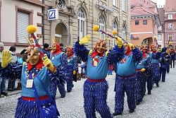 Mehrere Narren in gelb-grünen Kostümen gehen im Umzug und winken.