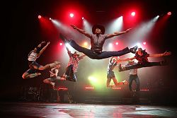 Mehrere junge Männer und Frauen springen mit angewinkelten oder gegrätschten Beinen hoch in die Luft