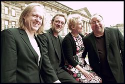 Das Bild zeigt das Ensemble "Sounds Of Change", drei Männer in schwarzen Anzügen und als zweite von rechts eine Frau in einem Blümchenkleid.