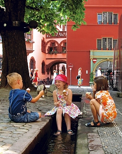 Die Stadt Lahr zeigt auf ihirer Homepage lohnenswerte Ausflugsziele der Region: Hier Freiburg. Das Bild zeigt die typischen Freiburger Bächle, an dem drei Kinder mit einem Eis spielen. 