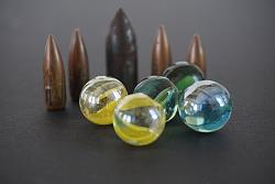 Das Foto zeigt bunte Murmeln, mit denen Kinder spielen können. Dahinter sind Patronen zu sehen. 