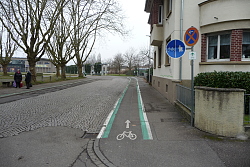 Das Bild zeigt einen getrennten Geh- und Radweg auf der rechten Straßenseite. Eine weiße senkrechte Linie trennt das blaue Verkehrsschild Geh- und Radweg. Zudem kennzeichnen auf dem Boden je eine weiße und eine grüne durchgezogene Linie rechts und links und ein weißes Rad-Piktogramm den Bereich für Radfahrer.