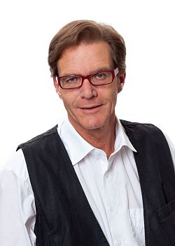 Portraitfoto von Gottfried Berger. Er hat braunes Haar und trägt eine rote Brille, außerdem ein weißes hemd mit einer schwarzen Weste.