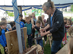 Mehrere Kinder stehen um Michael Heuberger,der einen Spalter hält, auf den ein Junge mit einem großen Holzhammer schlägt. 