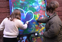 Zwei Mädchen besprühen eine Leinwand mit einem Graffiti