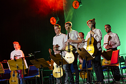 sechs Musiker mit ihren Gitarren bei einem Auftritt 
