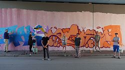 Eine Gruppe steht vor Graffiti-Kunst in einer Unterführung.