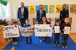 Gruppenbild mit Erster Bürgermeister Guido Schöneboom, Fabian Huber (BBBank) und Senja Töpfer (Amt für Soziales, Schulen und Sport) &#13;&#10;&#13;&#10;Davor vier Kinder die große Schilder halten, auf denen in großen Lettern steht: Danke BBBank für 46 gespendete Tablets. 