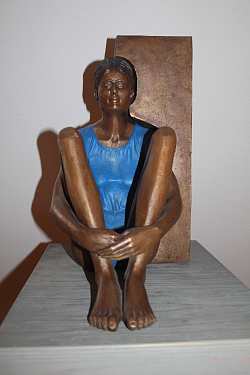 Zu sehen ist eine Metallskulptur des Künstlers Guido Messers. Dargestellt wird ein Mädchen, das mit angewinkelten Beinen auf einem Podest sitzt.