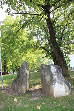 Skulptur aus zwei Teilen, wie ein gespaltener Felsbrocken, eingebettet in einer Grünfläche