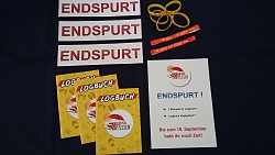 Auf dem Foto mit schwarzem Hintergrund sind verschiedene Materialien der Ferien-Lese-Aktion abgebildet, unter anderem drei der gelben Logbücher