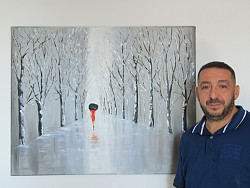 Zu sehen ist der Lahrer Künstler Hakim Azzaz neben seinem Ölgemälde. Dies zeigt eine schneebedeckte Allee, auf der eine Frau in einem Roten Kleid und mit schwarzem Regenschirm geht.