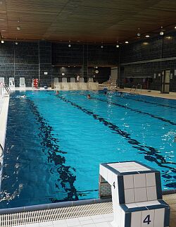 Innenaufnahme eines Schwimmerbeckens mit Startblöcken und mehreren Schwimmern im Wasser.