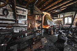 Innenraum einer historischen Hammerschmiede mit Schmiedewerkzeugen, Amboss, Schmiedefeuer und Holzbalkendecke.