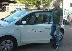Zu sehen ist Herbert Schneider, der an einem Fahrzeug des BGL auf dem Betriebsgelände steht. Er trägt ein dunkelgrünes Polo-Shirt, Jens und Turnschuhe.